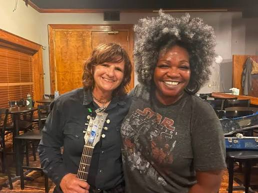 Trina Meade backstage with a guitarist holding an acoustic guitar