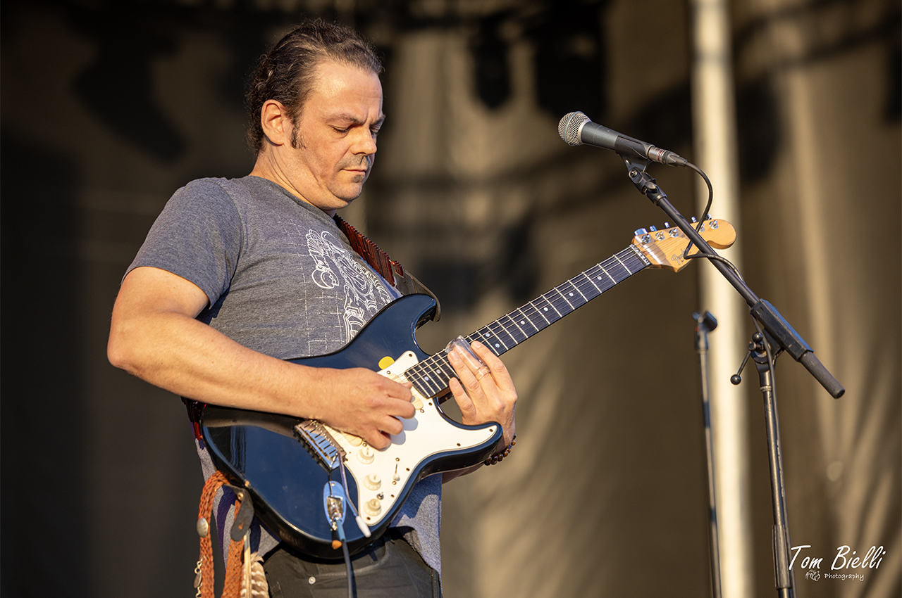 Daniel Groover playing a blue electric guitar on stage in golden light