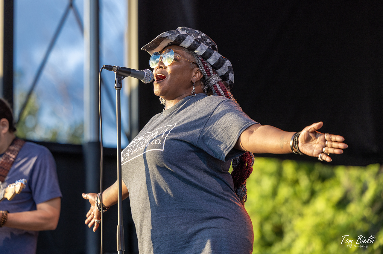 Trina Meade singing with arms wide open on an outdoor festival stage